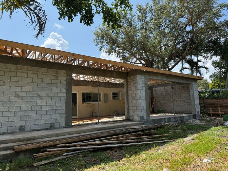 Residential addition in progress in Miami-Dade: concrete block walls, tie beam and wood roof trusses set over the new rooms